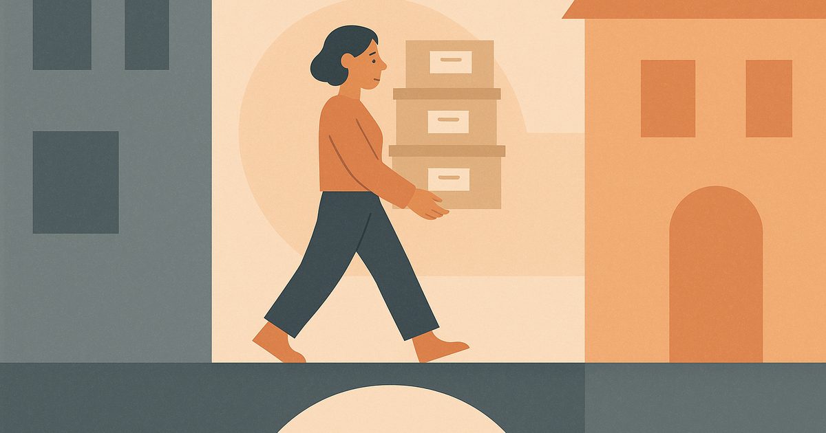 A person carries labeled filing boxes across a bridge from a grey building toward a warm orange building.
